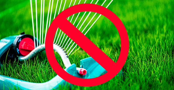 Sprinkler watering a lawn with a red prohibition symbol over it