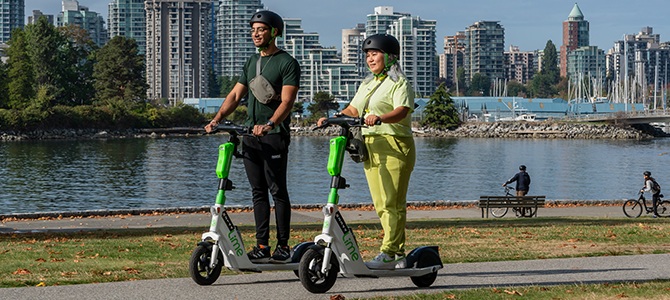 Two people riding Lime shared e-scooters along the Vancouver seawall.