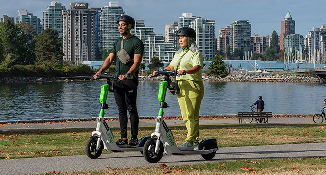 A man and a woman riding Lime e-scooters on the seawall