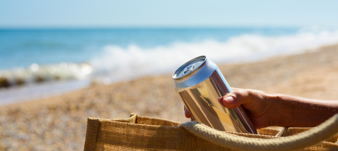 A person lifts a can from their bag on the beach