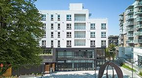 Front view of the completed Little Mountain building with ground-floor storefronts and apartments above.