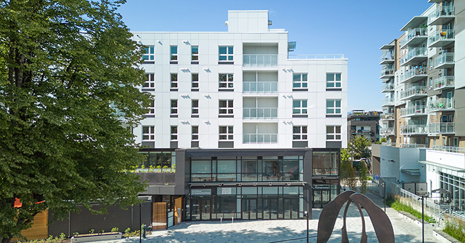Front view of the completed Little Mountain building with ground-floor storefronts and apartments above.