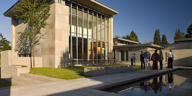 Celebration Hall at Mountain View Cemetery, featuring a modern building with tall glass windows, a reflection pool, and a small gathering of people outside.