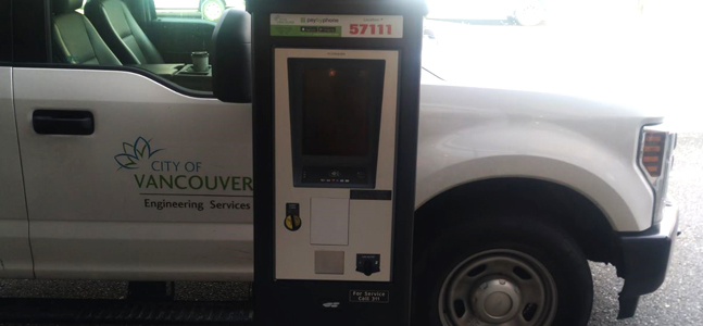 Pay parking terminal on a street with a truck in the background