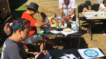 Two people sit outside and work on their art in the sunshine