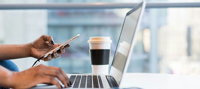 A women looks at her phone while on her computer