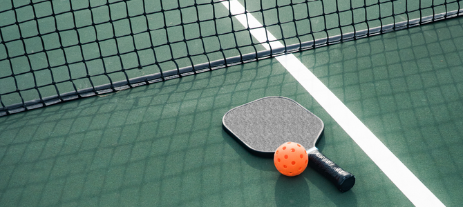 a black pickleball paddle and orange ball laying on top of a green pickleball court by the net 