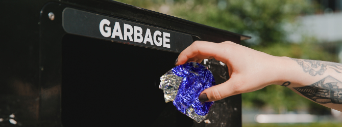 Someone placing their trash in a public garbage bin.