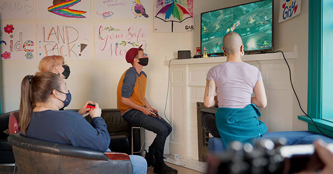 A small group of young adults gathered around a TV playing a video game.