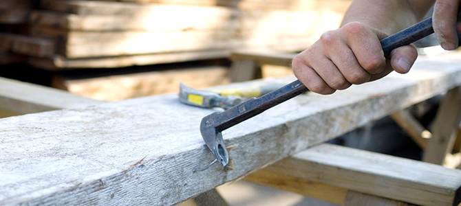 Person using a crowbar to remove nails from a wooden beam.