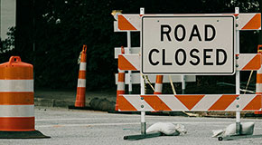 A road closed sign and orange cones around it