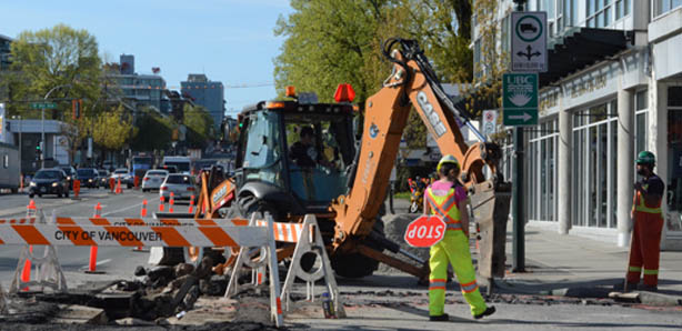 Construction workers with a stop sign and backhoe on city street