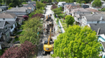 Aerial view of sewer upgrade construction on a residential street in the Shaughnessy area, with excavators, crews, and open trenches surrounded by houses and trees.