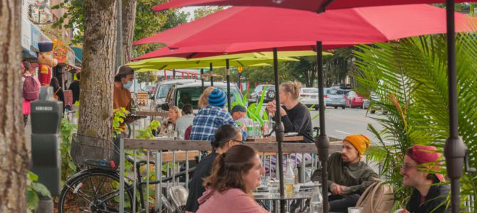 A lively street-side patio with people dining under umbrellas.
