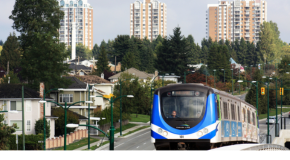 A skytrain runs away from a neighbourhood with buildings in the background