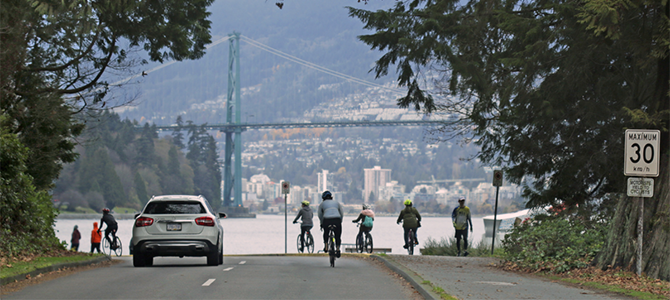 Cars and cyclists using Stanley Park Drive with Lions Gate Bridge in the background. 