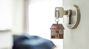 An open door leading to a room. On the door lock is a key with a keychain in the shape of a house. 