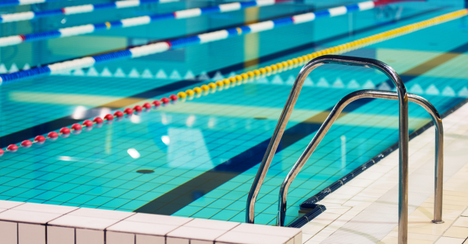 Indoor swimming pool featuring marked lanes with safety handrails in the foreground. 