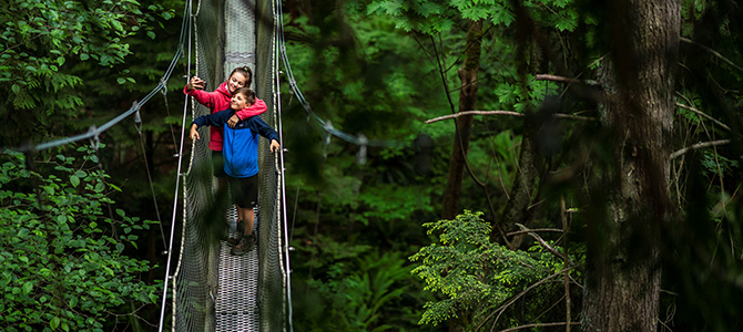 Two people posing for a selfie on a suspension bridge in the forest