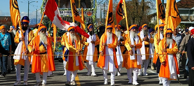 Participants in a Vaisakhi parade in Vancouver organized by the Khalsa Diwan Society, wearing orange robes and carrying Nishan Sahib flags and a Canadian flag