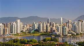 Skyline of downtown Vancouver on a clear summer day, with high-rise buildings in the foreground, sailboats in False Creek, and the North Shore Mountains in the background.