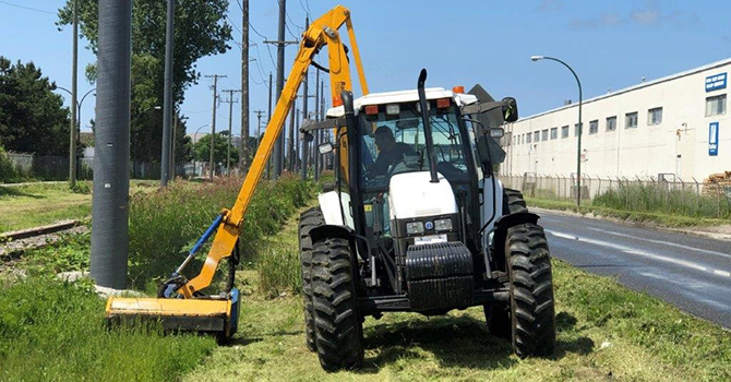 Staff use heavy equipment to prune vegetation on the side of the road.