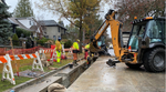 Construction workers in high-visibility clothing working on a residential street with a backhoe and safety barriers in Vancouver.