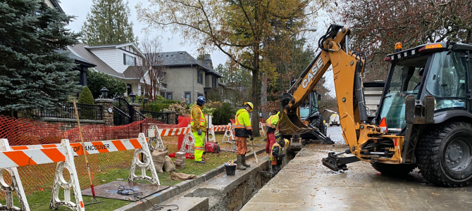 Construction workers in high-visibility clothing working on a residential street with a backhoe and safety barriers in Vancouver.