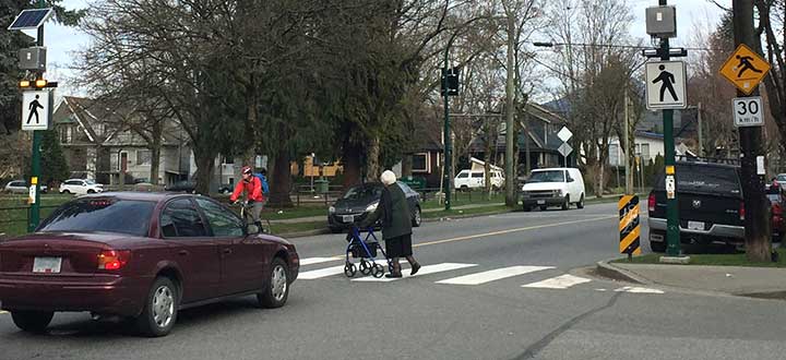 Car and cyclist stopped for pedestrian at crosswalk with flashing beacon at Victoria and Grant streets