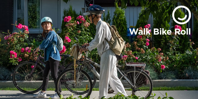 An elderly man and a young woman walking next to their bikes on the sidewalk