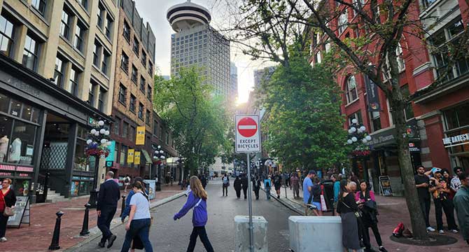 View of Water Street facing towards Harbour Centre, pedestrians standing and walking on the road.