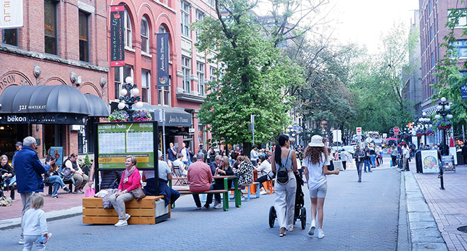 View of Water Street facing towards Harbour Centre, pedestrians standing and walking on the road.