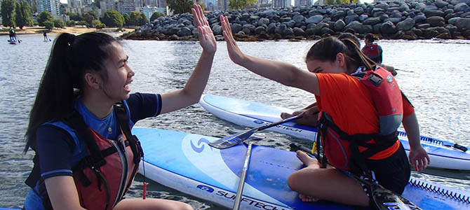 Two youth high-fiving while sitting on paddleboards