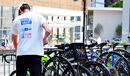 A man wearing a bike valet shirt with a row of locked bicycles