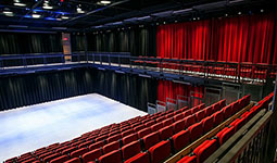 Interior view of the Annex Theatre showing red seating, a flexible open performance floor, black walls, and an upper balcony with additional seating.