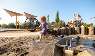 A child runs through the sandy area of the Champlain Heights playground on a sunny day.