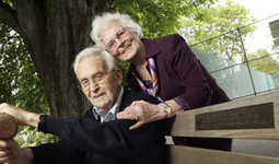 Older woman hugs her husband sitting on a park bench