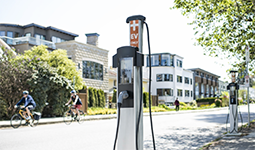 An EV station on a bright and busy street with cyclists passing by