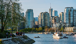 People walking along the False Creek seawall with boats on the water and downtown Vancouver in the background.