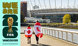 Vancouver’s FIFA World Cup 26™ poster with a man and child walking along the seawall toward BC Place, wearing Canadian flags on their backs.