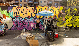 Artists painting a colourful mural on a wall along a city street.