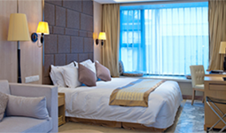 Furnished hotel room with a large bed, desk, chair, and a seating area by the window.