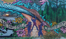 Mural on side of building of three people jumping on a sidewalk with the text: we take care of each other