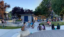 People siting at bench and picnic table with playground in the background