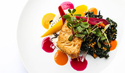 A beautifully plated dish featuring a grilled fillet, colorful vegetable garnishes, and vibrant sauces on a white plate