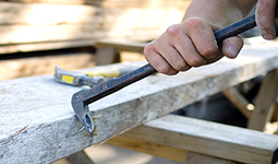 Person using a crowbar to remove nails from a wooden beam.
