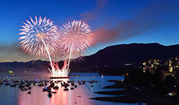 Fireworks over English Bay with boats on the water at dusk.