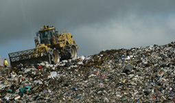 Large bulldozer compacting garbage at a landfill under cloudy sky