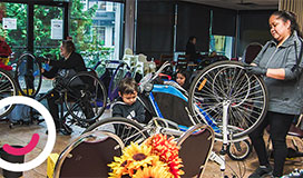 A group of people including children in a bike shop, looking at bike parts and inspecting their bike wheels