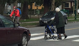 Car and cyclist stop at crosswalk as woman walks across street at crosswalk